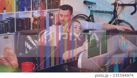 Reclining couple scrolling smartphone tablet on leather sofa at home with bicycle financial overlay 135594974