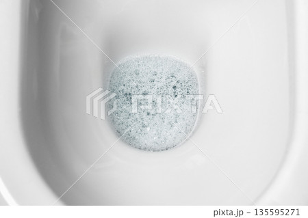 Clean water inside home toilet bowl covered with layer of blue disinfecting foamy bubbles. Aromatic cleaning treatment. Sanitary restroom scene Clean water inside home toilet bowl covered with layer of blue disinfecting foamy bubbles. Aromatic cleaning treatment. Sanitary restroom scene 135595271