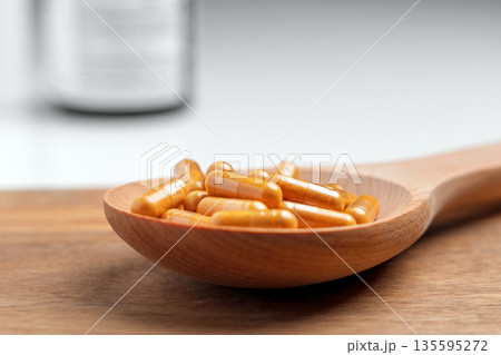Natural turmeric capsules with curcumin powder in a wooden spoon on rustic table background. Herbal dietary supplement.  Alternative medicine concept 135595272