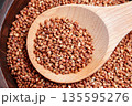 Raw buckwheat groats in a wooden spoon on a bowl filled with dry grains. Healthy cereal ingredient. Clean eating concept. Top view 135595276