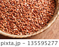 A wicker bowl full of dry uncooked buckwheat on a brown wooden table. Organic nutritious ingredient. 135595277