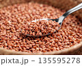 Metal spoon scooping uncooked buckwheat grains. Food storage concept 135595278
