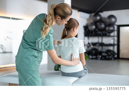 Female physio in medical uniform helping girl during exercise Female physio in medical uniform helping girl during exercise 135595775