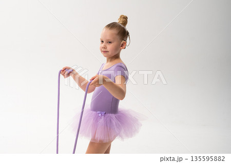 Young ballerina with cochlear implant looking at rope in her hands. Copy space. Symbol of awareness, concentration, and childhood inclusion through art and technology. Young ballerina with cochlear implant looking at rope in her hands. Copy space. Symbol of awareness, concentration, and childhood inclusion through art and technology. 135595882