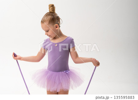 Young dancer with a cochlear implant holds a rope in profile during ballet training. Copy space. Inclusive movement, auditory support, and physical development through rhythmic gymnastics and dance Young dancer with a cochlear implant holds a rope in profile during ballet training. Copy space. Inclusive movement, auditory support, and physical development through rhythmic gymnastics and dance 135595883