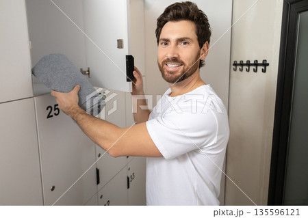 Dark-haired bearded man taking a towel out of locker in gym Dark-haired bearded man taking a towel out of locker in gym 135596121