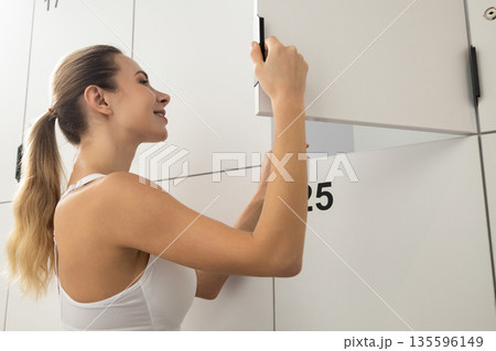 Long-haired blonde woman in a gym changing room opening the locker 135596149
