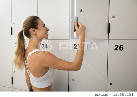 Long-haired blonde woman in a gym changing room opening the locker 135596151