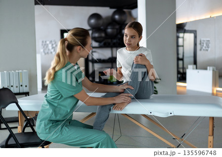Physiotherapist helping young girl perform knee exercise 135596748