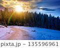 winter solstice landscape with snow covered country road winding through forest in mountains. day and night time change concept. alpine countryside with sun and moon. duality and transition template 135596961