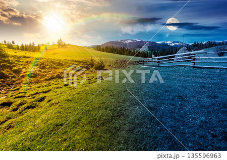 rural landscape in spring. day and night time change concept. haystack near fence on meadow with sun and moon at twilight. forest on rolling hills. mountain with snow tops. equality and shift template 135596963