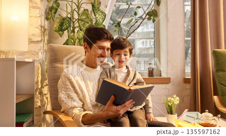 Father reading book aloud to young son at home. 135597162