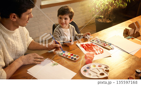 Dad and son painting together at table with watercolors. 135597168