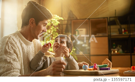 Father and son talking while playing with modeling clay indoors. Father and son talking while playing with modeling clay indoors. 135597171
