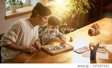 Father and son playing with modeling clay at wooden table. 135597191