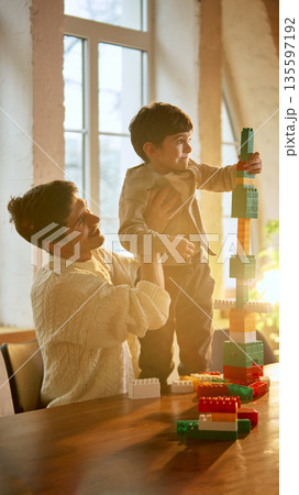Father lifting son while stacking colorful toy blocks. Father lifting son while stacking colorful toy blocks. 135597192