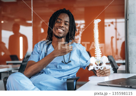 Holding and showing model of human spine. Black man doctor is in the office 135598115