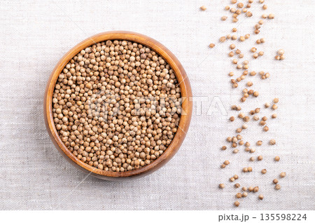 Coriander seeds, whole and dried, in a wooden bowl on linen. Fruits of Coriandrum sativum, a spice with lemony citrus flavor, due to the terpenes linalool and pinene, that enhances when roasted. Photo Coriander seeds, whole and dried, in a wooden bowl on linen. Fruits of Coriandrum sativum, a spice with lemony citrus flavor, due to the terpenes linalool and pinene, that enhances when roasted. Photo 135598224