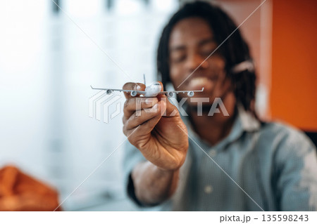 Focused view of toy plane, airline company. Black businessman is working in office 135598243