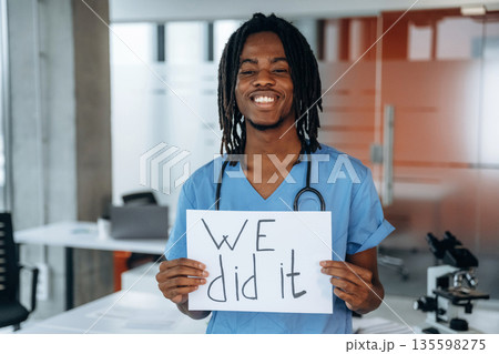 Holding paper with text 'we did it'. Black man doctor is in the office Holding paper with text 'we did it'. Black man doctor is in the office 135598275