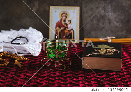 A burning Orthodox lamp, a Bible, a cross with a chain, and an icon on the table A burning Orthodox lamp, a Bible, a cross with a chain, and an icon on the table 135599045