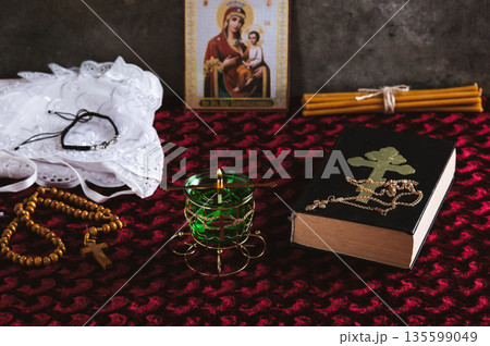A lamp, rosary beads, a Bible, an Orthodox icon and a cross for prayer on a red table A lamp, rosary beads, a Bible, an Orthodox icon and a cross for prayer on a red table 135599049