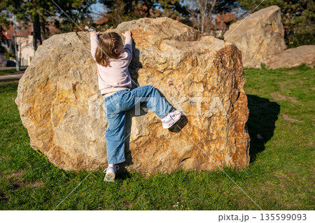 Little girl jumping on decorative stones in city park. Active spring play and outdoor childhood lifestyle. 135599093