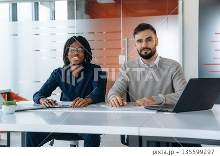 Looking at the camera, sitting. Two men are working in the office Looking at the camera, sitting. Two men are working in the office 135599297