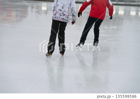 Man and woman skating side by side on clean ice rink during winter, back view. Concept of companionship, winter activity and shared healthy lifestyle Man and woman skating side by side on clean ice rink during winter, back view. Concept of companionship, winter activity and shared healthy lifestyle 135599586