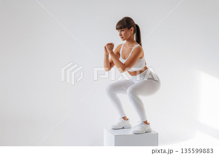 Doing squats. Young sportive woman is in the studio Doing squats. Young sportive woman is in the studio 135599883