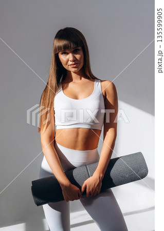 Yoga mat in hands. Young sportive woman is in the studio 135599905