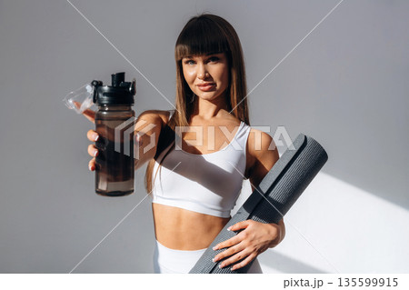 Taking a break, with bottle of water. Young sportive woman is in the studio Taking a break, with bottle of water. Young sportive woman is in the studio 135599915