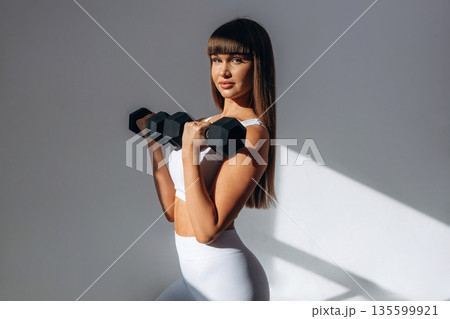 Black dumbbells in hands. Young sportive woman is in the studio 135599921