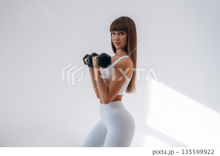 Black dumbbells in hands. Young sportive woman is in the studio 135599922