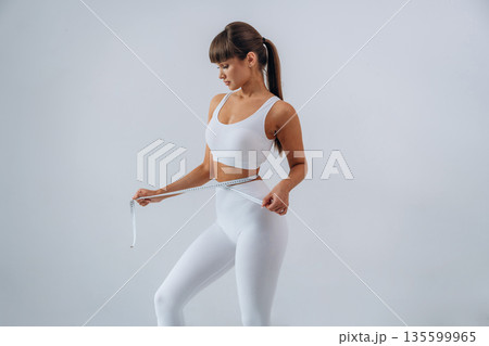 Diet conception, measuring tape. Young sportive woman is in the studio Diet conception, measuring tape. Young sportive woman is in the studio 135599965