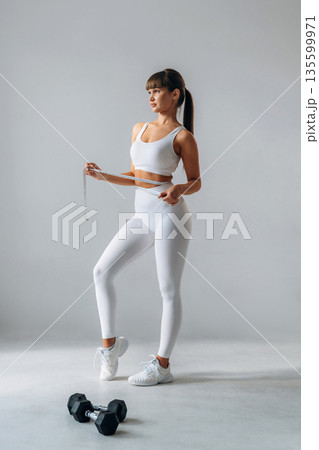 Against white wall. Young sportive woman is in the studio Against white wall. Young sportive woman is in the studio 135599971