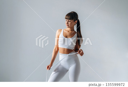 Measuring the waist. Young sportive woman is in the studio 135599972