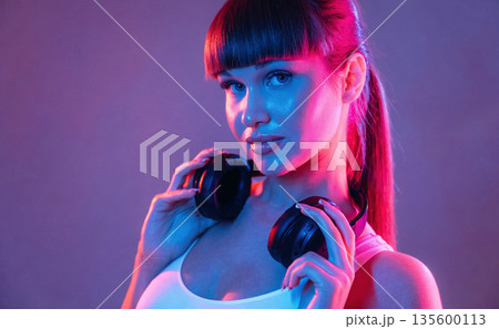 Headphones on the neck. Young sportive woman is in the studio 135600113