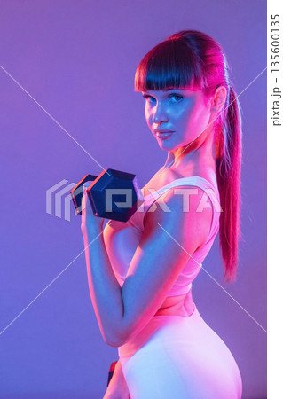 Arms exercise using dumbbell. Young sportive woman is in the studio Arms exercise using dumbbell. Young sportive woman is in the studio 135600135