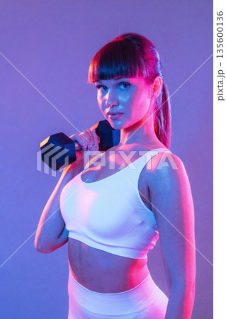 Arms exercise using dumbbell. Young sportive woman is in the studio Arms exercise using dumbbell. Young sportive woman is in the studio 135600136