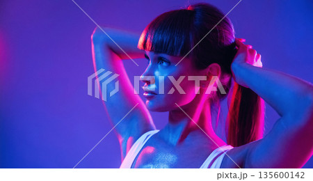 Touching her hair, standing and posing. Young sportive woman is in the studio 135600142