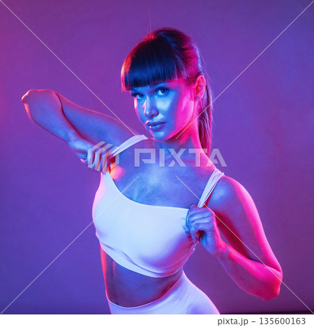 Neon lighting, showing the top. Young sportive woman is in the studio Neon lighting, showing the top. Young sportive woman is in the studio 135600163