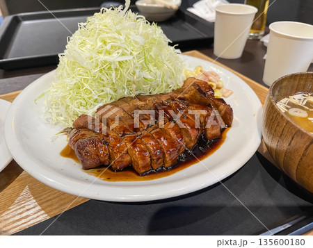 千切りキャベツとトンテキ。甘いタレをかけた豚肉の料理。 135600180