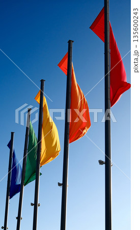 Colorful flags waving on tall poles against clear blue sky Colorful flags waving on tall poles against clear blue sky 135600243