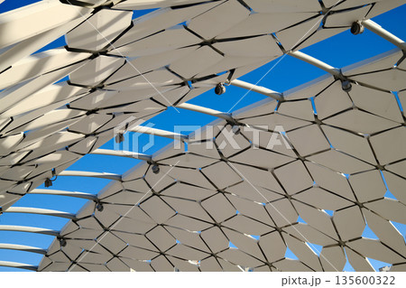 Futuristic architectural canopy roof with geometric panels, modern public space design, abstract structure against blue sky 135600322
