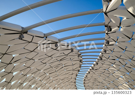Futuristic architectural canopy roof with geometric panels, modern public space design, abstract structure against blue sky 135600323
