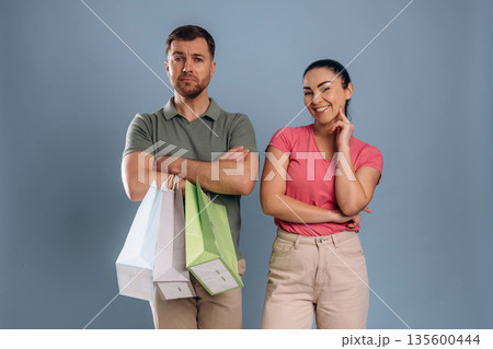 Guy is unsatisfied, holding shopping bags. Man and woman are in the studio Guy is unsatisfied, holding shopping bags. Man and woman are in the studio 135600444