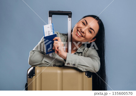 With a suitcase, passport and plane tickets. Beautiful woman is against background 135600570