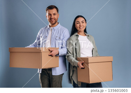 Against blue wall, with boxes, moving. Man and woman are in the studio 135601003
