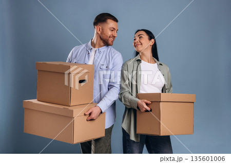Against blue wall, with boxes, moving. Man and woman are in the studio Against blue wall, with boxes, moving. Man and woman are in the studio 135601006